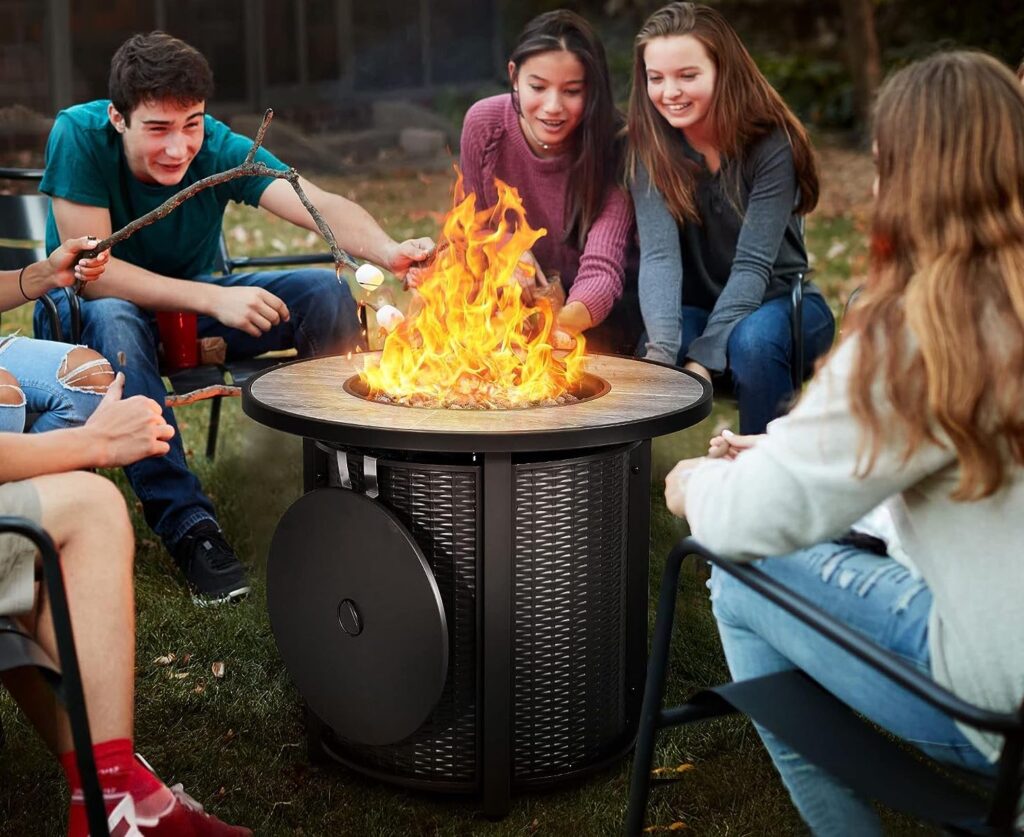 Young men and women toasting marshmallows around a round fire pit table.