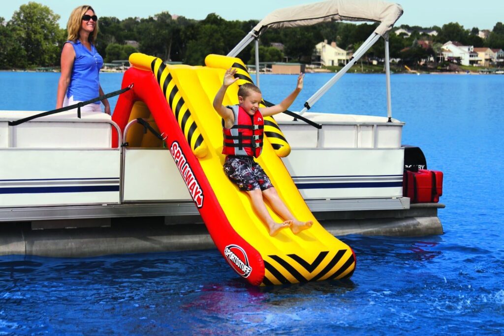 Inflatable slide on a pontoon boat with a boy sliding down into the water.