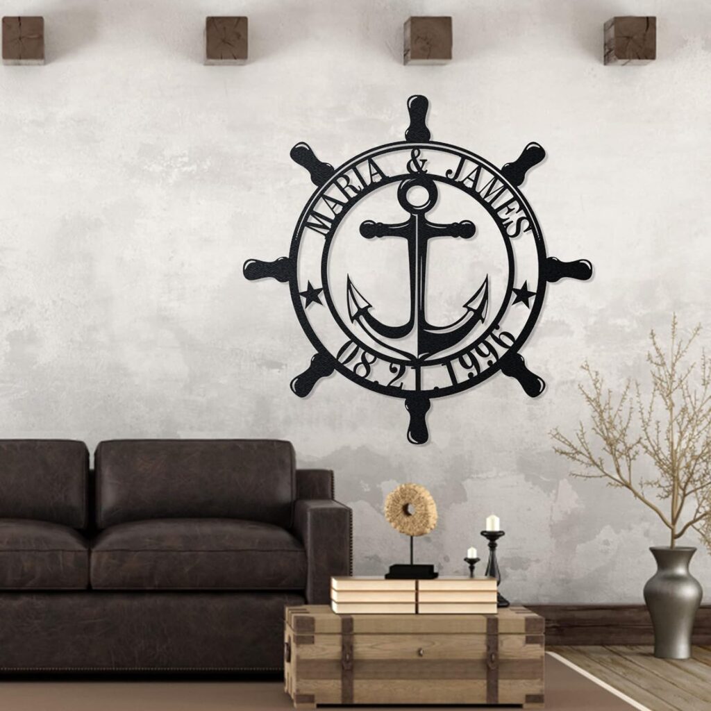 A black silhouette of a ship's wheel with an anchor in the middle. It is customized with two names and dates. The piece of nautical decor is mounted to a wall above a couch.