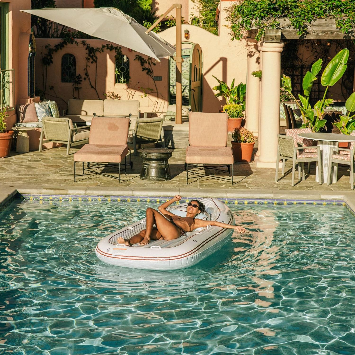 A tan, attractive woman in a bikini laying on a Funboy luxury yacht inflatable pool float.